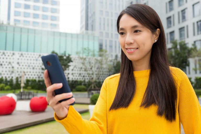 Smiling woman using her smartphone outdoors, symbolising Mocean SMS Messaging Campaign Web Portal for simple and effective customer communication in the Philippines.